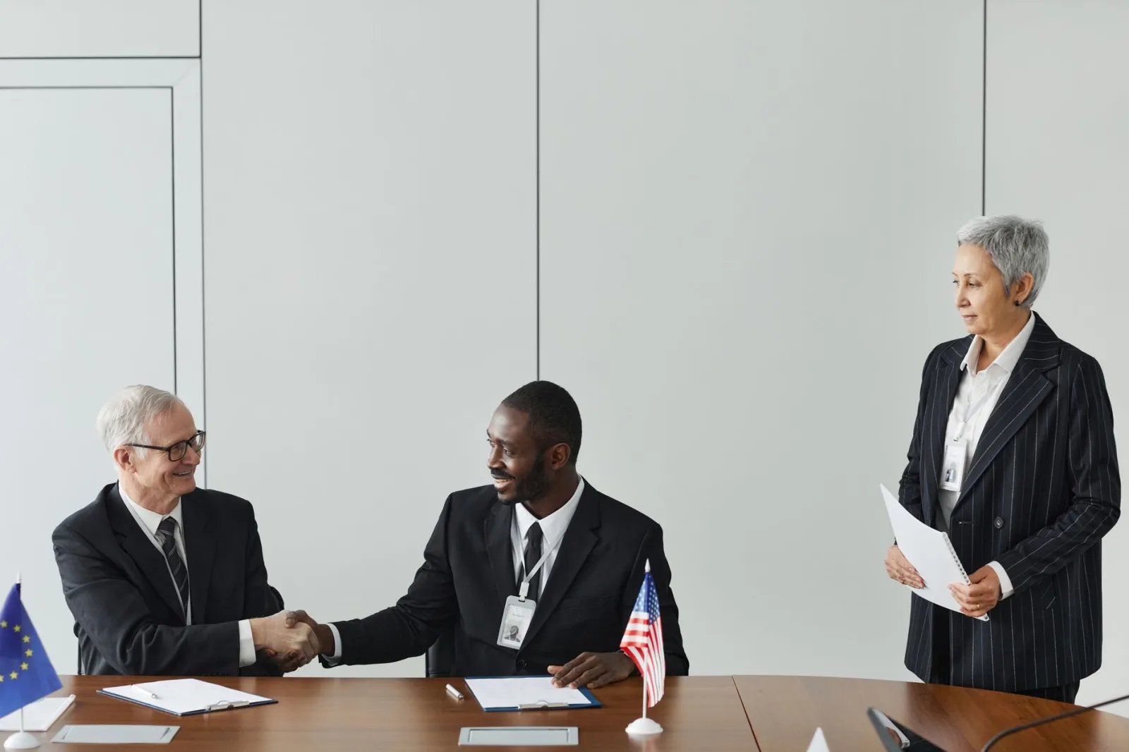 Multinational business meeting with agreement signing, featuring diverse professionals and flags.