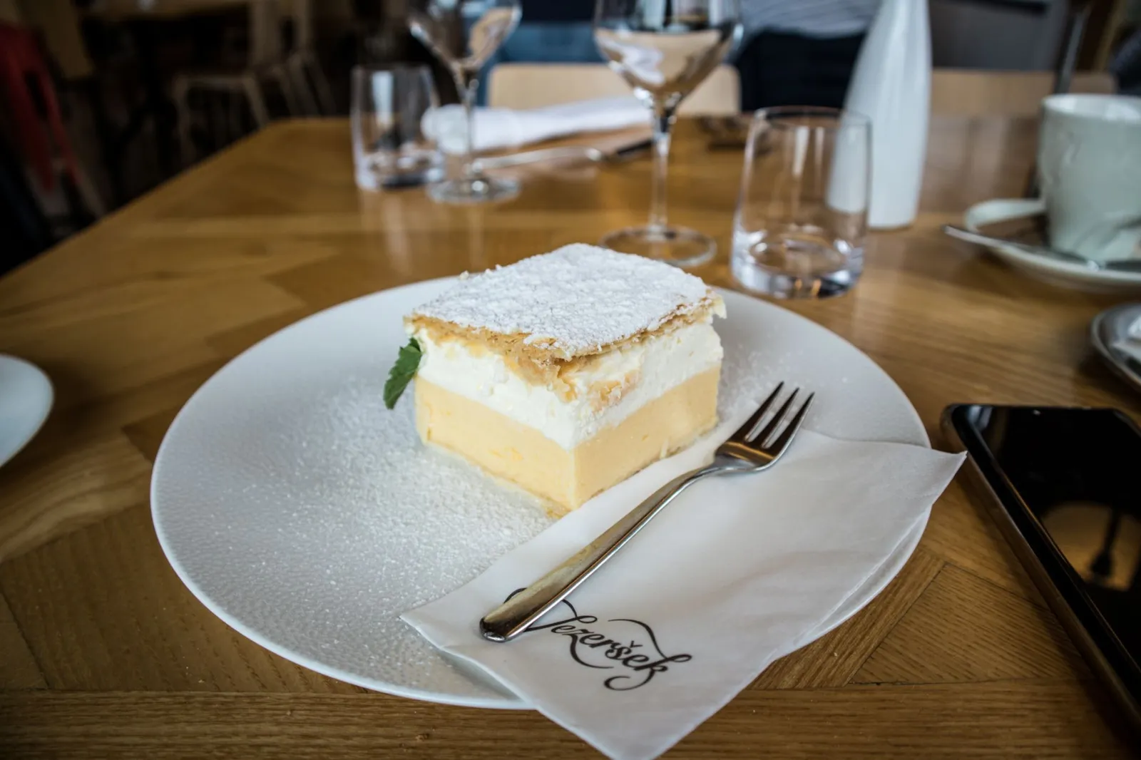 A scrumptious layered cream cake topped with powdered sugar, served on an elegant table setting.