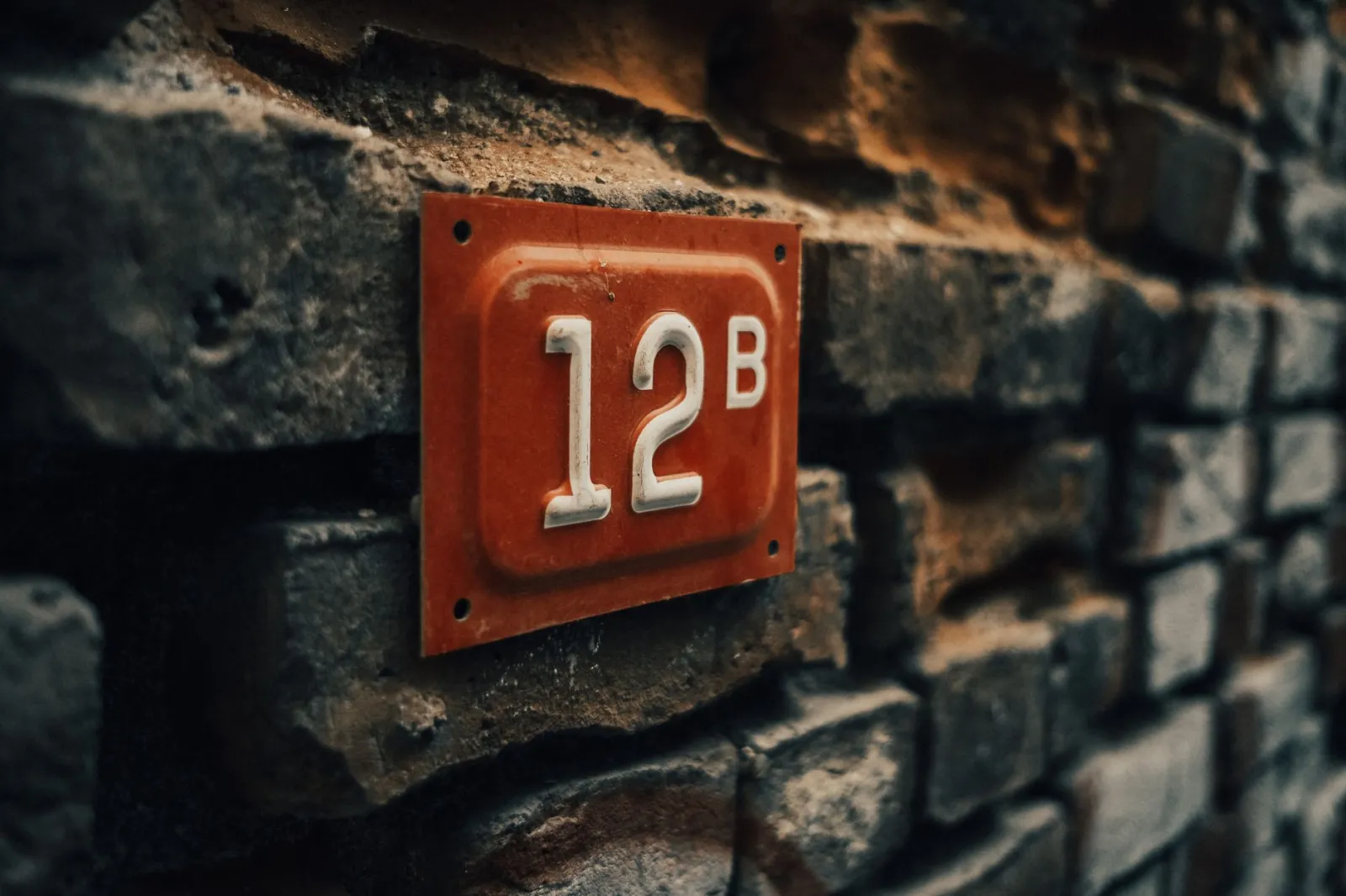 Close-up of a vintage apartment number 12B on a textured stone wall.