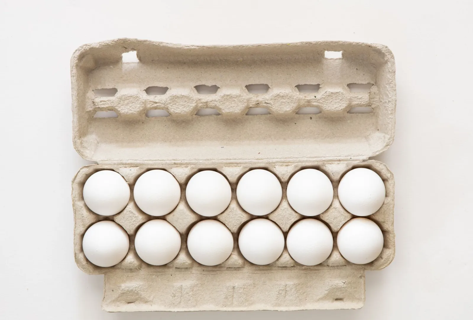 Minimalist flat lay of white eggs in a carton tray, perfect for culinary or health concepts.